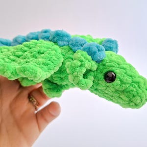 Peut inclure: Un dragon en crochet vert fait &agrave; la main avec des d&eacute;tails bleus. Le dragon a un aspect textur&eacute; et moelleux, avec un &oelig;il fonc&eacute;. Les ailes et le dos sont orn&eacute;s de touffes bleues. Un jouet doux et fantaisiste.