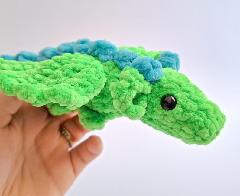 Peut inclure: Un dragon en crochet vert fait &agrave; la main avec des d&eacute;tails bleus. Le dragon a un aspect textur&eacute; et moelleux, avec un &oelig;il fonc&eacute;. Les ailes et le dos sont orn&eacute;s de touffes bleues. Un jouet doux et fantaisiste.