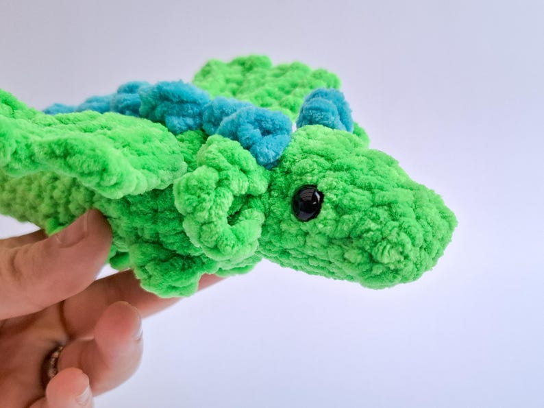 Peut inclure: Un jouet dragon en peluche fait &agrave; la main, vert vif avec des accents bleu sarcelle. Le dragon a un aspect textur&eacute; et flou, un &oelig;il noir et est tenu dans une main. Ce jouet doux convient aux enfants.