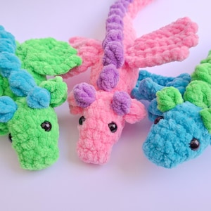 Peut inclure: Trois dragons au crochet color&eacute;s en vert, rose et bleu. Chaque dragon a de grands yeux noirs, des ailes et un aspect textur&eacute; et moelleux. Les dragons sont faits &agrave; la main et conviennent aux enfants.