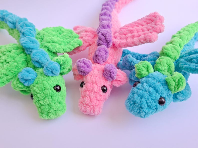 Peut inclure: Trois dragons au crochet color&eacute;s en vert, rose et bleu. Chaque dragon a de grands yeux noirs, des ailes et un aspect textur&eacute; et moelleux. Les dragons sont faits &agrave; la main et conviennent aux enfants.