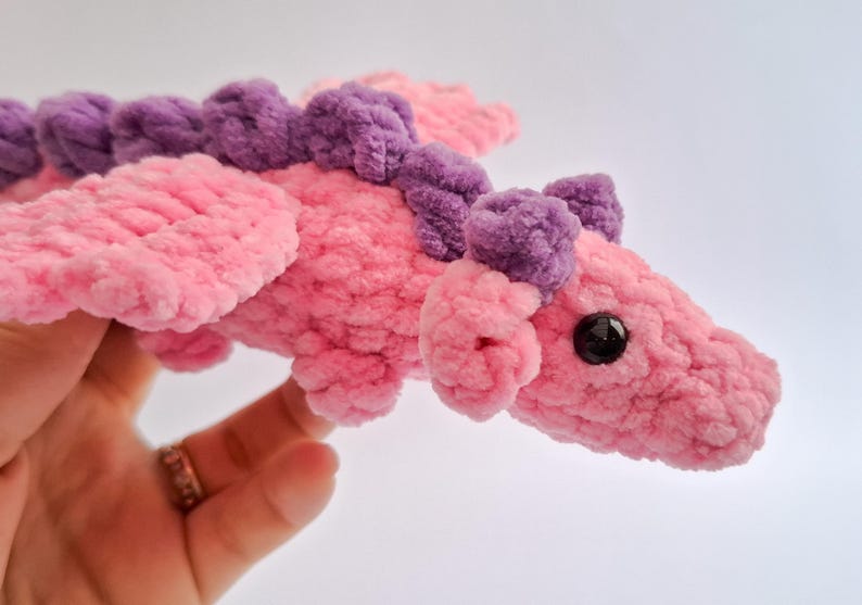 Peut inclure: Un jouet dragon en peluche fait &agrave; la main, rose et violet. Le dragon pr&eacute;sente un corps, des ailes et des &eacute;l&eacute;ments d&eacute;coratifs textur&eacute;s et flous. Il a un &oelig;il noir et est con&ccedil;u pour &ecirc;tre doux et c&acirc;lin.