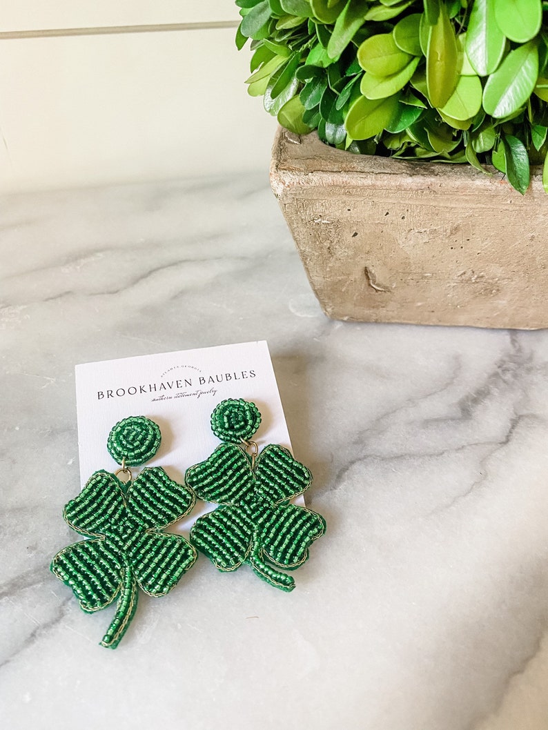 May include: Green beaded clover earrings with gold accents. The earrings are on a white card with the text "BROOKHAVEN BAUBLES" and "handmade statement jewelry".