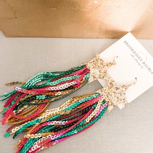 May include: Gold star-shaped earrings with long, colorful fringe made of sequins. The fringe is a mix of green, pink, orange, and gold sequins.