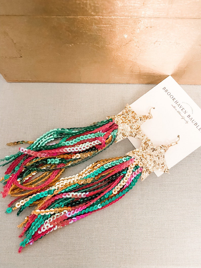 May include: Gold star-shaped earrings with long, colorful fringe made of sequins. The fringe is a mix of green, pink, orange, and gold sequins.