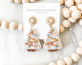 May include: White beaded Christmas tree earrings with colorful beads and gold accents. The earrings are on a white card with the text "Brookhaven Baubles" and "subtle statement jewelry".
