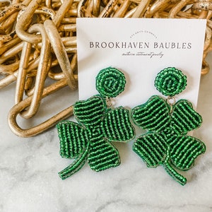 May include: Green beaded clover earrings with a gold accent. The earrings are displayed on a white card with the text "Brookhaven Baubles, Southern Statement Jewelry".