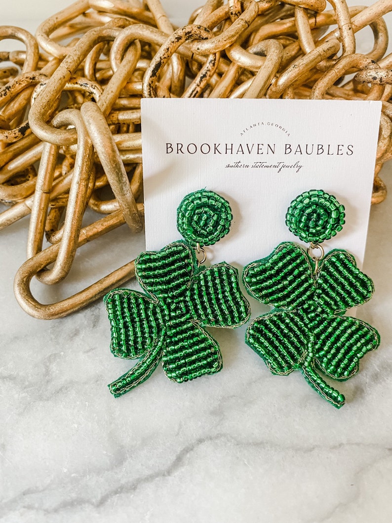 May include: Green beaded clover earrings with a gold accent. The earrings are displayed on a white card with the text "Brookhaven Baubles, Southern Statement Jewelry".