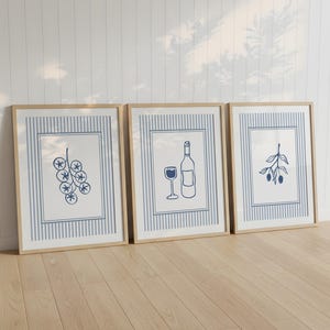 May include: Three framed art prints with botanical and wine-themed illustrations. Each print features a blue and white striped border. The images depict a bunch of grapes, a wine bottle and glass, and an olive branch, all in blue line art.