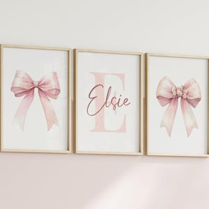 May include: Three framed prints with watercolor bows and the name "Elsie". The bows are a soft pink with delicate details. The middle print features a large pink letter "E" and the name "Elsie" in a matching script.