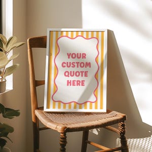 May include: A framed print with the text "YOUR CUSTOM QUOTE HERE" in a pink and white design. The print has a white frame and is set against a yellow and white striped background. The print is displayed on a wooden chair.