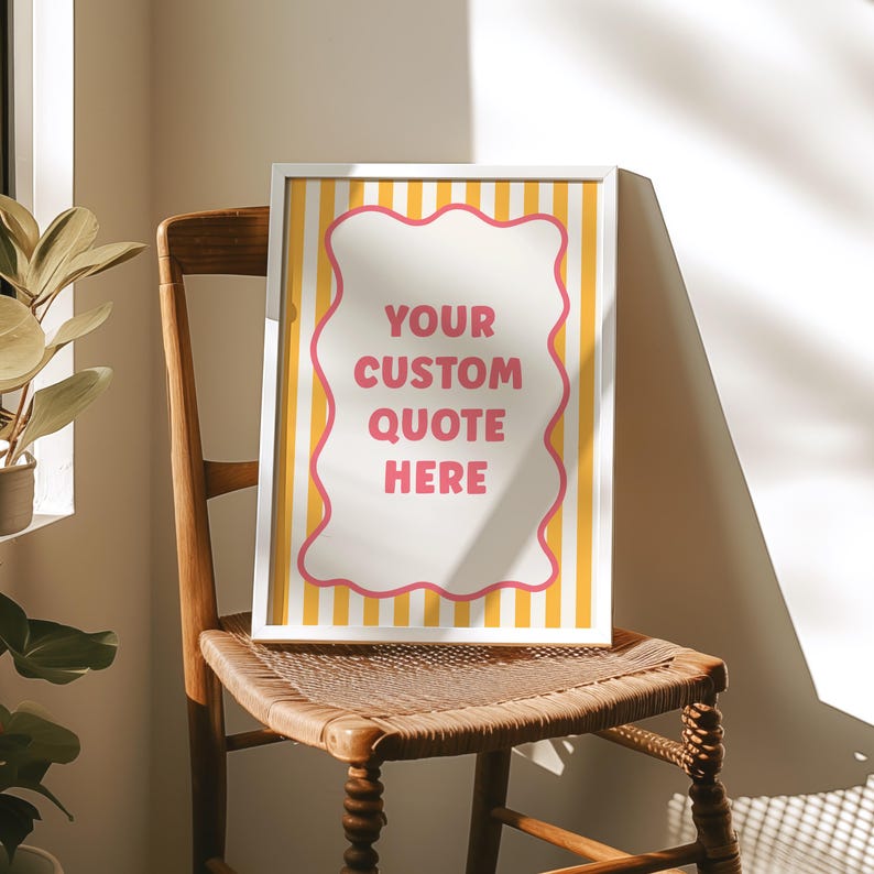 May include: A framed print with the text "YOUR CUSTOM QUOTE HERE" in a pink and white design. The print has a white frame and is set against a yellow and white striped background. The print is displayed on a wooden chair.