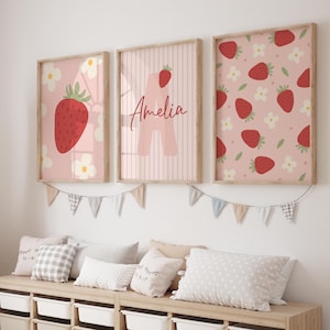 May include: Three framed art prints with a strawberry theme. One print features a large strawberry and white flowers on a pink background. Another has the name "Amelia" and a strawberry. The third print displays a strawberry pattern.