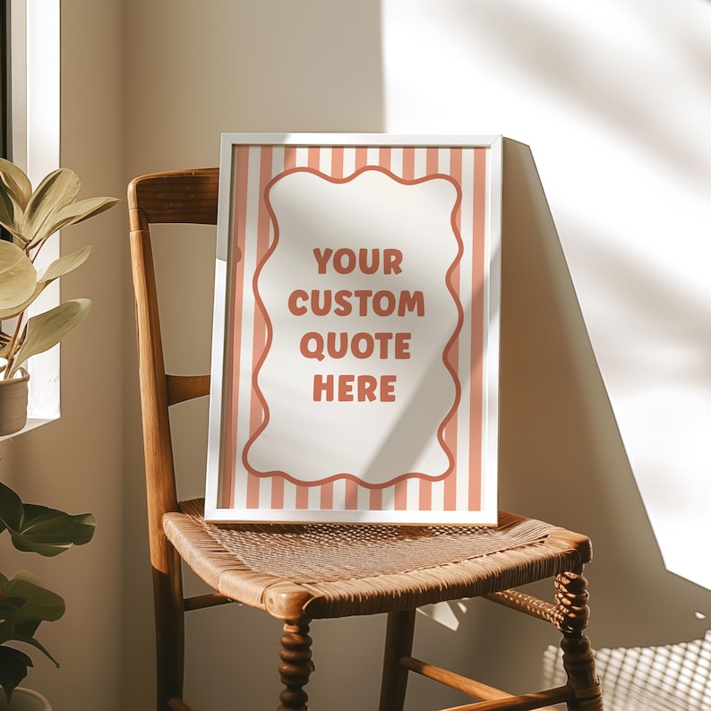 May include: A framed print with the text "YOUR CUSTOM QUOTE HERE" in a white, wavy-edged shape, set against a background of vertical peach stripes. The frame is white. The print rests on a wooden chair with a woven seat.