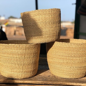 May include: Three woven baskets made of natural materials, stacked on top of each other. The baskets are a light brown color and have a natural, rustic look.