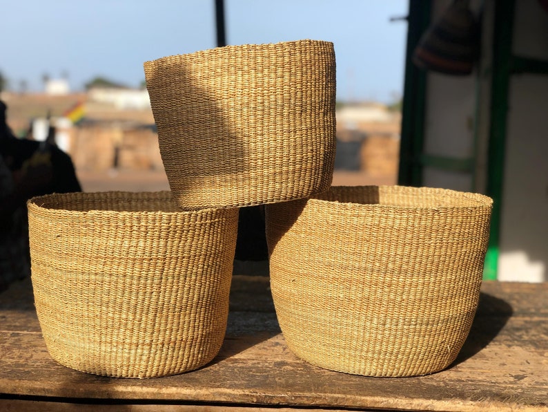 May include: Three woven baskets made of natural materials, stacked on top of each other. The baskets are a light brown color and have a natural, rustic look.