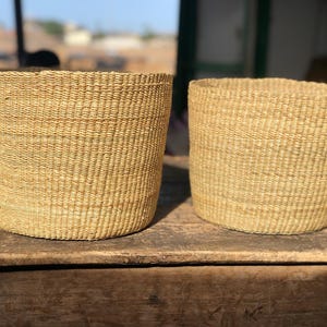 May include: Two woven baskets made of natural fibers, with a light brown color. The baskets are cylindrical in shape and have a slightly textured surface.
