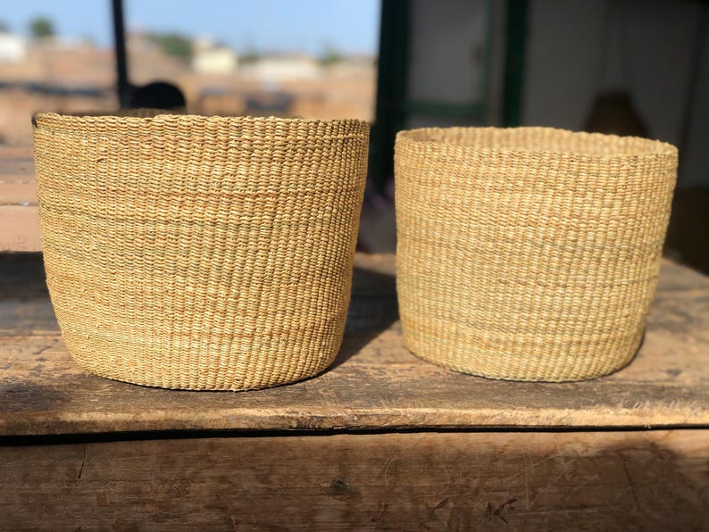 May include: Two woven baskets made of natural fibers, with a light brown color. The baskets are cylindrical in shape and have a slightly textured surface.