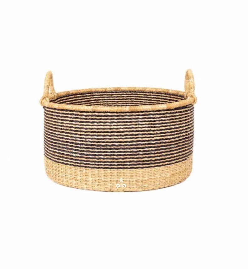 May include: A large, round, woven storage basket with black and natural colored stripes. The basket has two handles and a natural colored base.