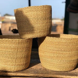 May include: Three woven baskets made of natural materials, stacked on top of each other. The baskets are a light brown color and have a natural, rustic look.