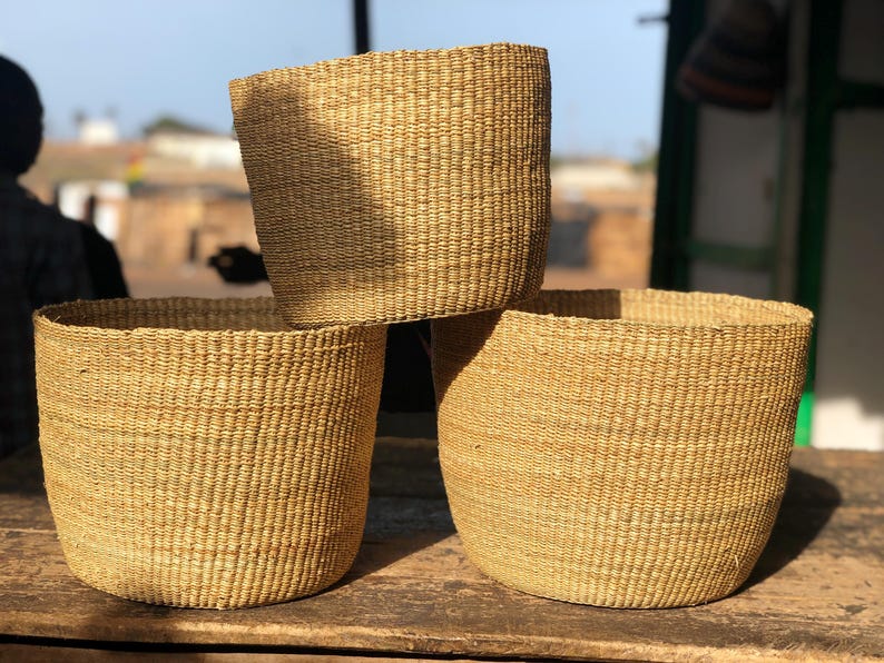 May include: Three woven baskets made of natural materials, stacked on top of each other. The baskets are a light brown color and have a natural, rustic look.