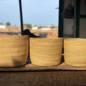 May include: Three woven baskets made of natural materials, with a light brown color. The baskets are sitting on a wooden surface.