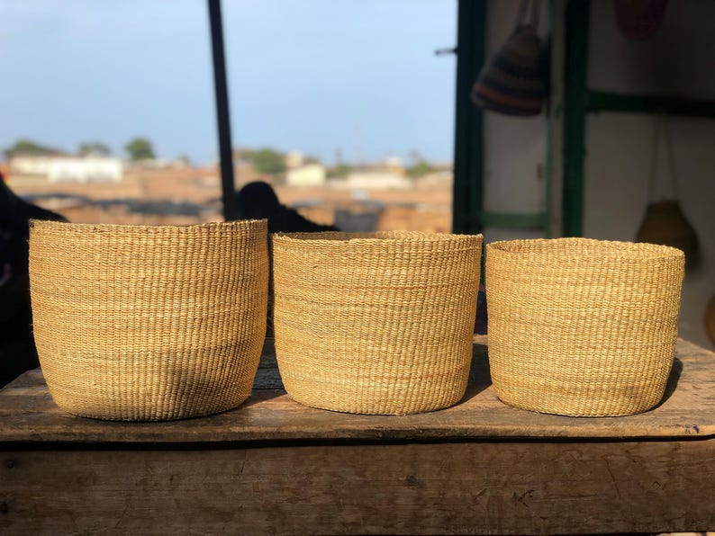 May include: Three woven baskets made of natural materials, with a light brown color. The baskets are sitting on a wooden surface.