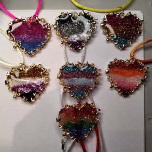 Peut inclure: Sept colliers en forme de cœur avec des chaînes dorées et des cœurs en résine remplis de paillettes. Chaque cœur présente une combinaison de couleurs différente, notamment le rose, le bleu, le blanc, le noir, l'orange et le vert.