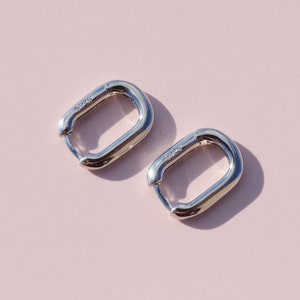 May include: A pair of silver hoop earrings with a rectangular shape. The earrings are made of metal and have a smooth finish.