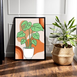 Peut inclure: Une affiche encadrée représentant une plante Monstera dans un pot blanc, sur un fond abstrait de formes orange et beige. L'impression est encadrée en noir. L'œuvre a un thème botanique et convient à la décoration intérieure.