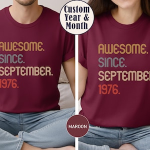 May include: A maroon t-shirt featuring the text AWESOME. SINCE. SEPTEMBER. 1976. in a multi-colored, retro-inspired font. The word AWESOME is in yellow, SINCE is in grey, SEPTEMBER is in light orange, and 1976 is in a bold red-orange color.