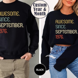 May include: A black long-sleeve sweatshirt featuring the text "AWESOME. SINCE. SEPTEMBER. 1976." printed in a multi-colored retro font. The design includes a circular badge stating "Custom Year & Month" and a circular label indicating the color is black.