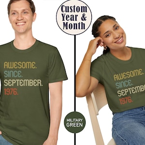 May include: A military green short-sleeve t-shirt featuring the text "AWESOME. SINCE. SEPTEMBER. 1976." printed in a stacked, multi-colored retro font on the chest. The design uses shades of tan, light blue, and orange for the lettering.