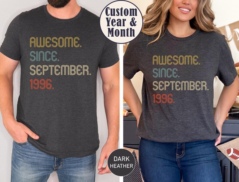 May include: A dark heather gray short-sleeve t-shirt featuring the text "AWESOME. SINCE. SEPTEMBER. 1996." printed in a retro-style font with gold, teal, and red colors. The shirt has a crew neckline and a standard fit, showcasing a vintage-inspired design.