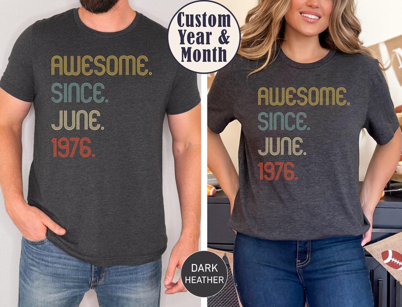 May include: Dark heather gray t-shirts with the text "AWESOME. SINCE. JUNE. 1976." in retro-style lettering. The shirts are worn by two people, one male and one female. The text is in yellow, teal, and red.