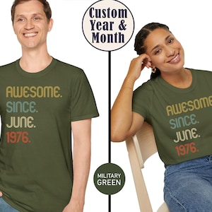 May include: Two people wearing olive green t-shirts. The shirts have the text "AWESOME. SINCE. JUNE. 1976." in a retro font. The text "Custom Year & Month" is in a circle above the shirts. The shirts are military green.
