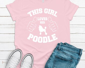 May include: Pink t-shirt with white text that reads "This Girl Loves Her Poodle" with two thumbs up on either side of the text and a poodle silhouette in the center.