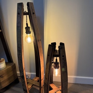 Puede incluir: Dos lámparas de pie de madera hechas con barriles de vino reciclados, con un diseño rústico e industrial. Cada lámpara tiene una sola bombilla colgando de un cable negro.
