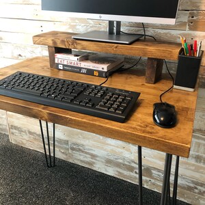 May include: A rustic wooden desk with hairpin legs, a computer monitor on a wooden stand, a keyboard, a mouse, and a black pencil holder with coloured pencils. The desk is made of reclaimed wood and has a natural finish.