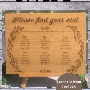 Puede incluir: Un letrero de madera con el texto "Por favor, encuentre su asiento" y un plano de asientos para una boda. El letrero est&aacute; cortado con l&aacute;ser de chapa de roble real y presenta un dise&ntilde;o floral.