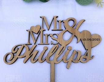 Puede incluir: Topper de pastel de madera con las palabras "Mr & Mrs Phillips" y la fecha "10.09.2021" en forma de corazón.