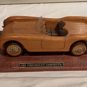 May include: A wooden model of a 1953 Chevrolet Corvette on a wooden base with a plaque that reads "1953 Chevrolet Corvette".