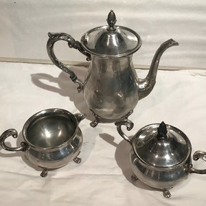 May include: A silver tea set comprising a teapot, creamer and sugar bowl. Each piece features a decorative design and stands on three feet.