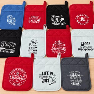 May include: A collection of eleven square quilted pot holders in blue, red, black, and white. Each features a unique white or black graphic print with kitchen-themed phrases like Kiss the Cook, Baking is my Jam, and I Bake What's Your Superpower.