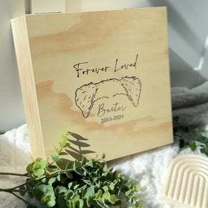 May include: A wooden box with a personalized inscription that reads "Forever Loved" with a dog illustration and the name "Baxter" and the dates "2015-2024".