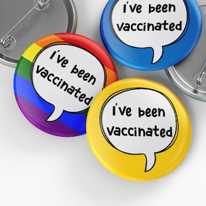 Könnte beinhalten: Vier runde Knöpfe mit dem Text "Ich bin geimpft" in einer Sprechblase. Die Knöpfe sind blau, gelb, regenbogenfarben und silber.