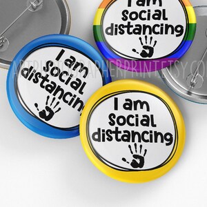 May include: Three round buttons with the text "I am social distancing" and a handprint. The buttons are blue, yellow, and rainbow.