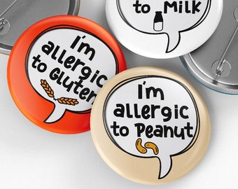 May include: Four round button pins with white speech bubbles and black text. The text on the buttons reads "I'm allergic to Milk", "I'm allergic to Gluten", "I'm allergic to Peanut", and the back of one button is visible.