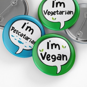 May include: Three round button pins with speech bubbles. The first pin is green and says "I'm Vegetarian". The second pin is blue and says "I'm Pescatarian". The third pin is green and says "I'm Vegan".