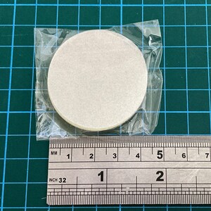 K&ouml;nnte beinhalten: Eine Packung runde, cremefarbene Papierfilter, etwa 3,8 cm im Durchmesser, ist in einem durchsichtigen Plastikbeutel versiegelt. Die Filter liegen auf einer gr&uuml;nen Rasteroberfl&auml;che mit einem Lineal zur Ma&szlig;stabsbestimmung.